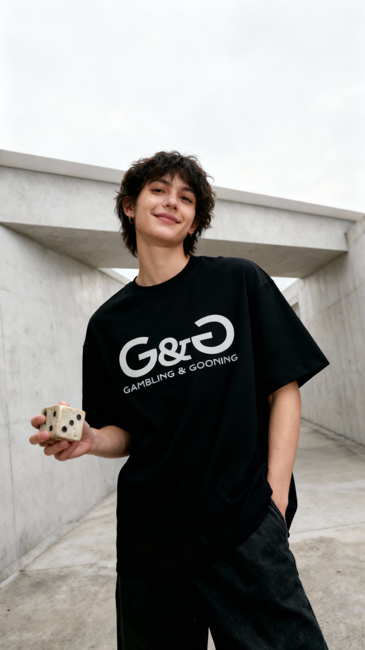 Ragazzo sorridente con maglietta nera G&G Gambling & Gooning tiene dado gigante in mano in ambiente urbano